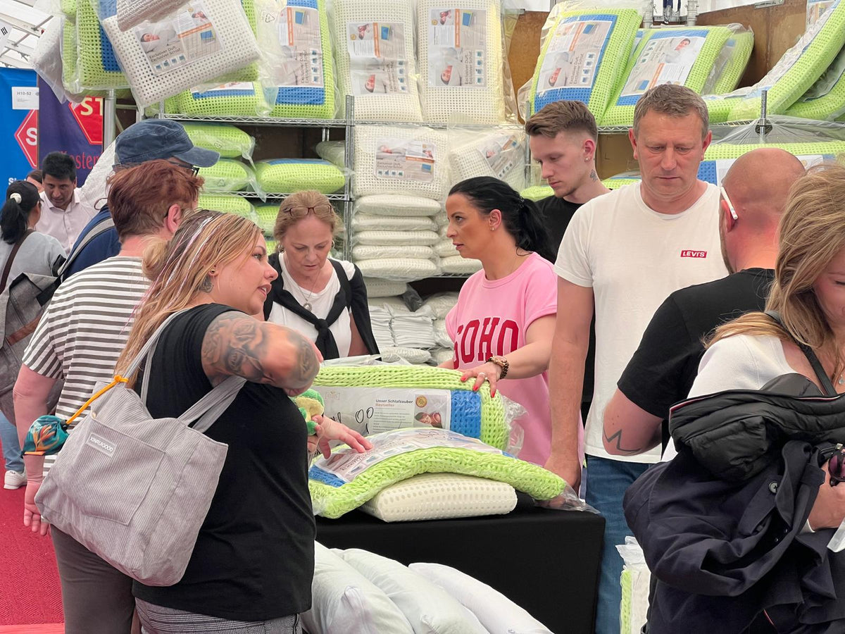Kundinnen und Kunden lassen sich am Tisch das Schlafzauber-Kissen zeigen