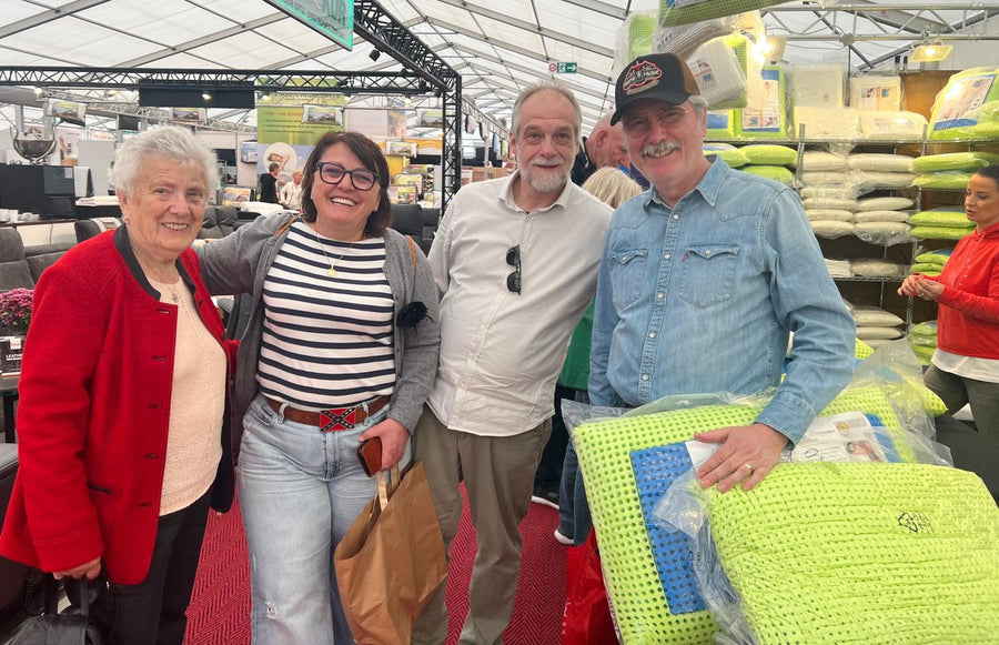 Vier lachende Kunden am Messestand, einer hält ein verpacktes Schlafzauber-Kissen in der Hand