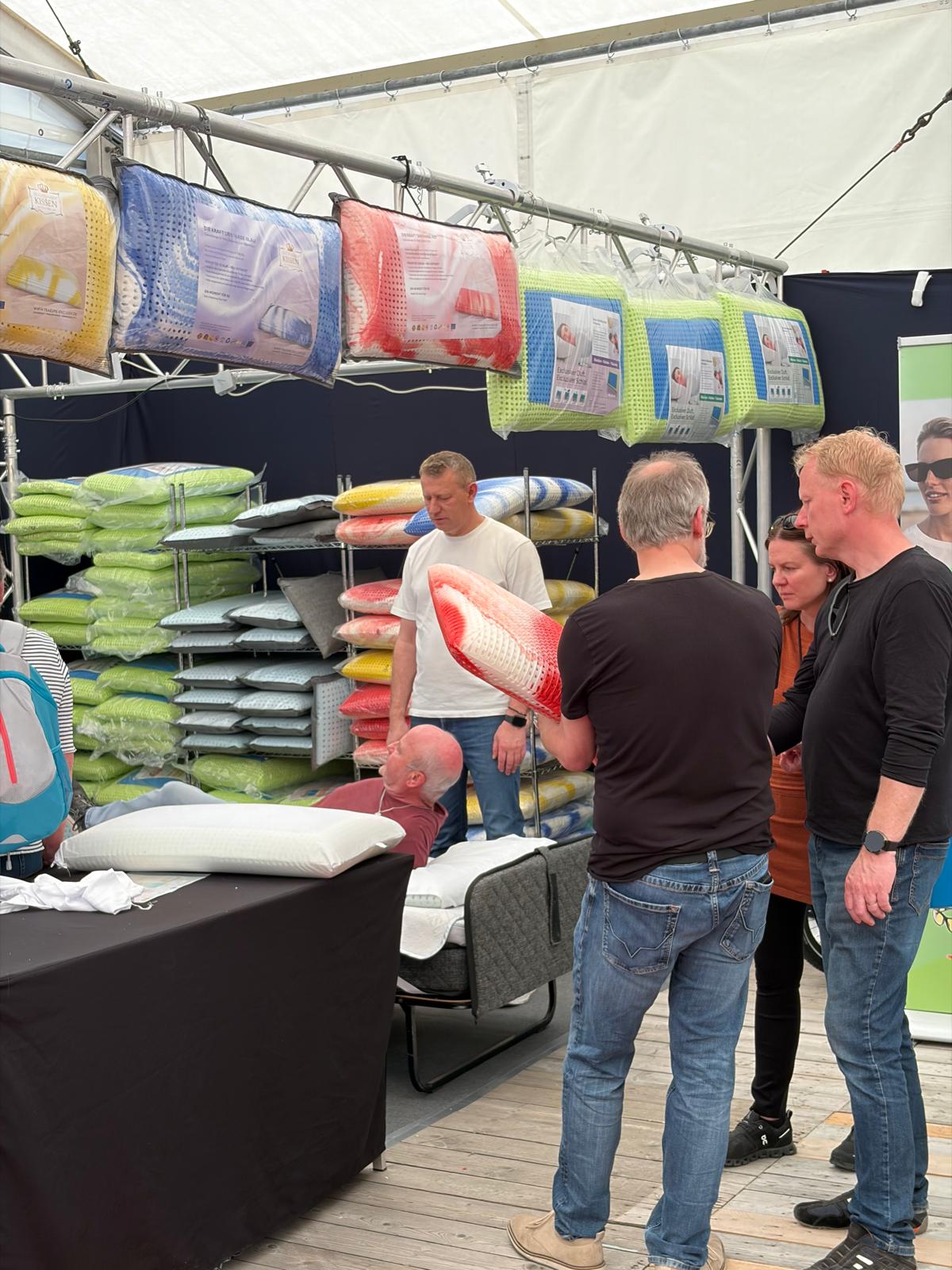 Probeliegen am Messestand vor wartenden Besuchern, im Hintergrund die Regale mit Schlafzauber-Kissen